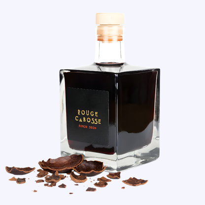 Bouteille Rouge Cabosse® 50 cl, bouteille cubique design posée sur des éclats de fèves de cacao, illustrant la fusion naturelle entre vin rouge et cacao.