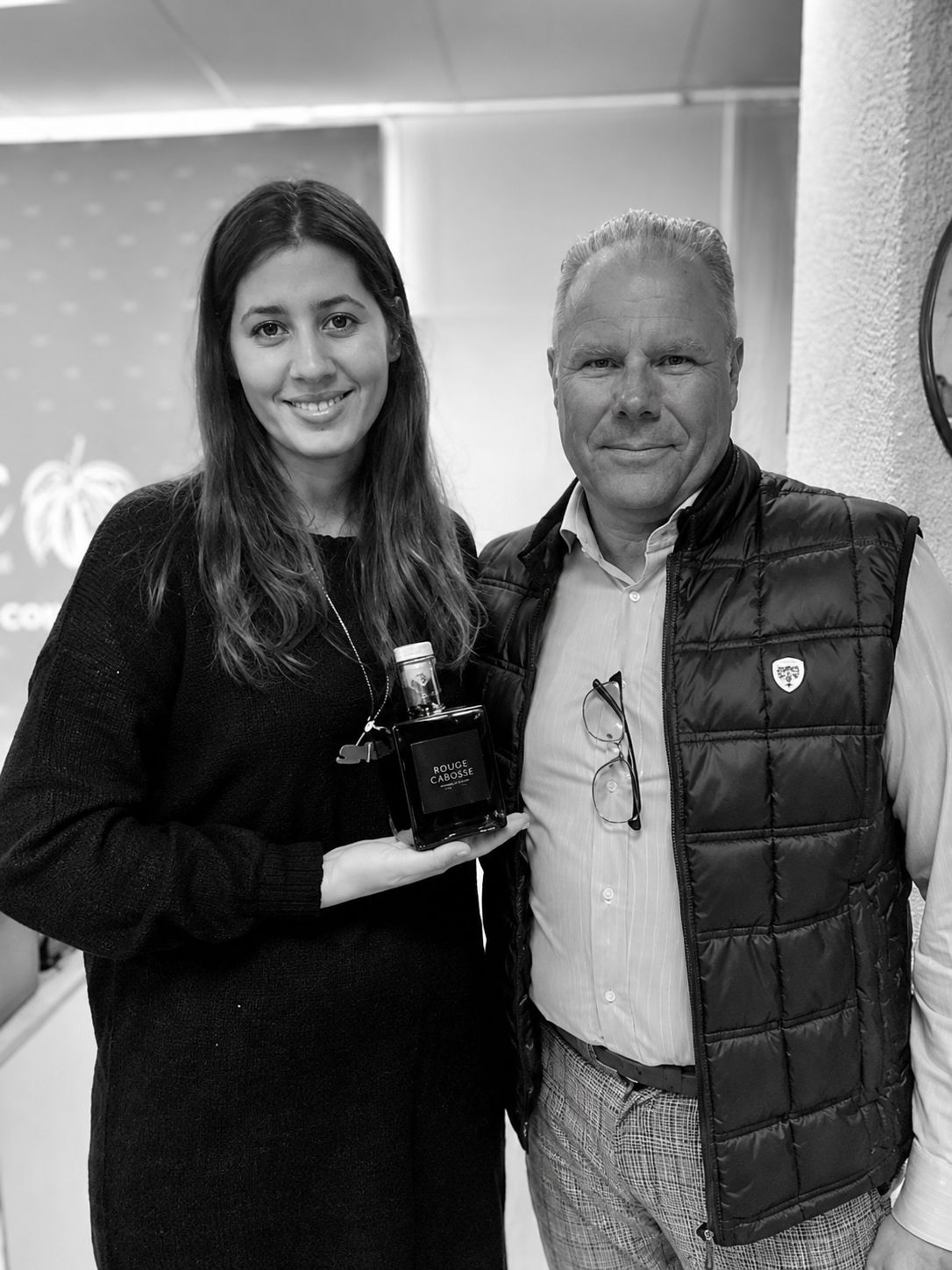 photo en noir et blanc de Fréderic CHANAL le dirigeant de la société de INNO WINE à coté de Hasnaâ Ferreira élu tablette d'or 2024 et championne du monde du chocolat en 2026 , tenant dans sa main une bouteille rouge cabosse. 