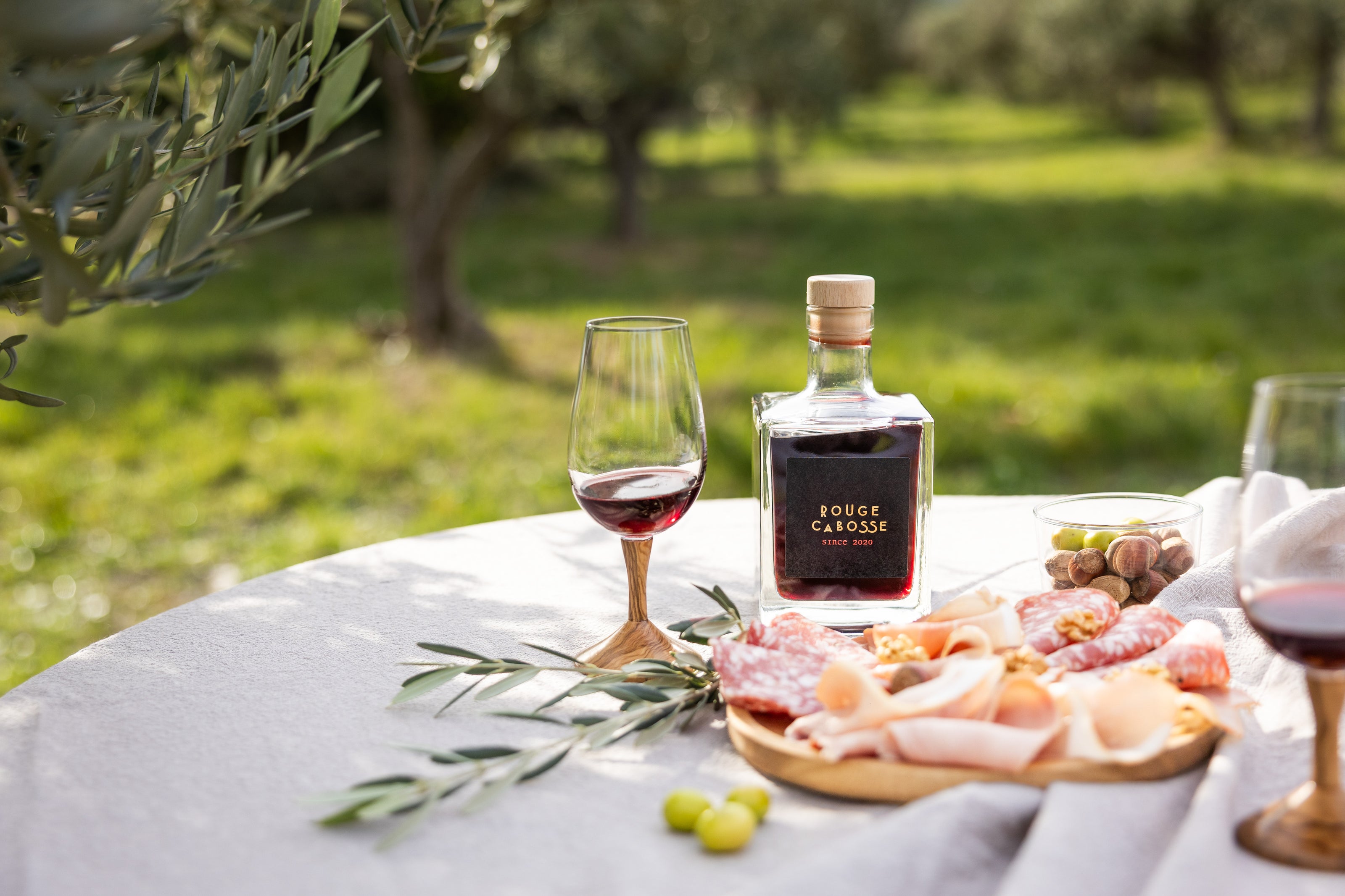 bouteille de rouge cabosse entouré d'un plateau de charcuterie et de branches d'oliviers 
